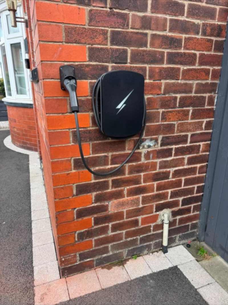 Hypervolt EV charge point mounted beside the corner of a red brick house in Ruislip, lead stowed on a holster on the return wall.
