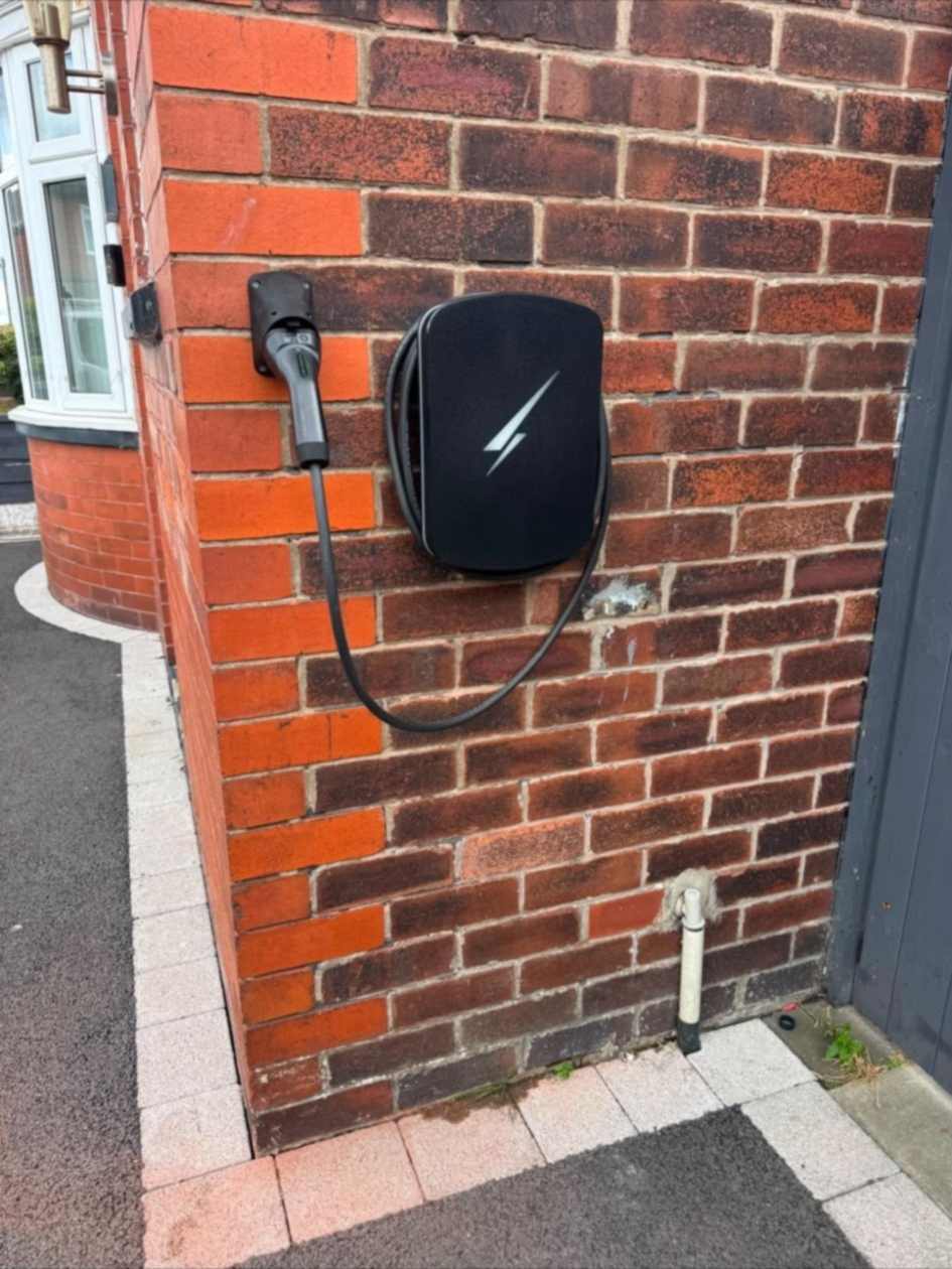 Hypervolt EV charge point mounted beside the corner of a red brick house in Ruislip, lead stowed on a holster on the return wall.