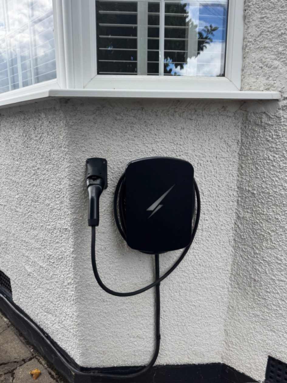 Black Hypervolt charge point on a white rendered wall in South Ruislip, charging lead coiled around the unit with the connector docked in a holster beside it.