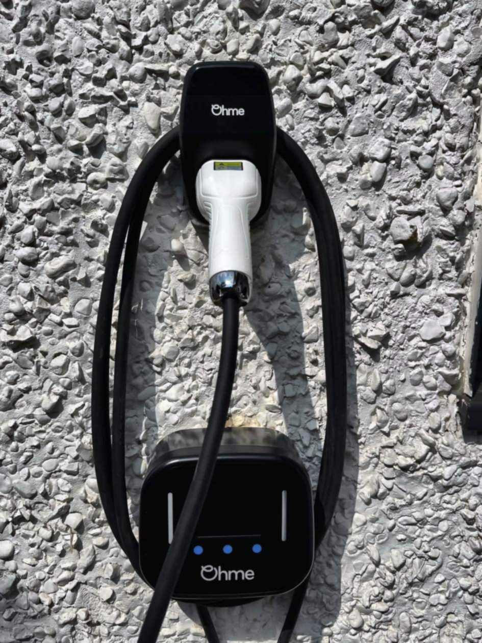 Ohme EV charge point on a white pebbledash rendered wall, with the tethered lead coiled around the unit and the plug docked in a wall holster above. EV charger installation in Chalfont.