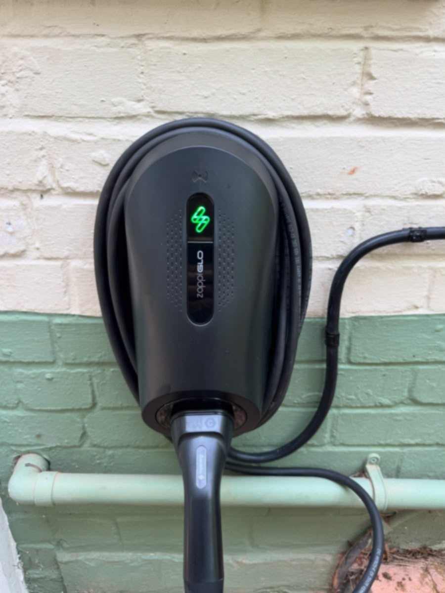 myenergi zappi GLO EV charge point mounted on a painted brick wall, cable neatly coiled on the unit. EV charger installation in Beaconsfield.